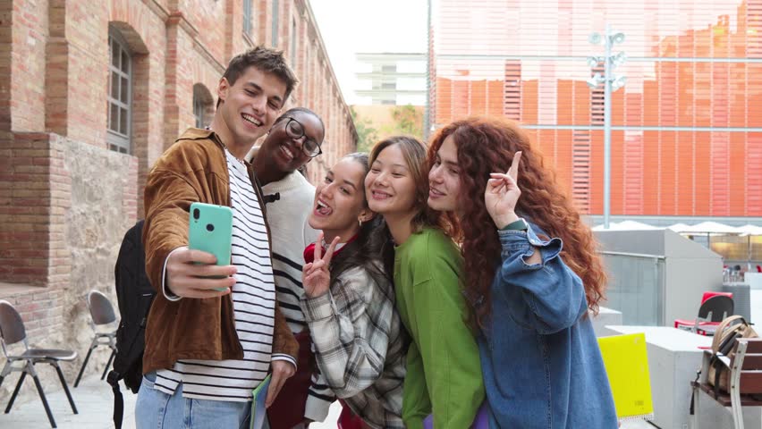 Young teenage student taking a selfie with his cool friends using a smart phone. Group of multiracial classmates taking a portrait with a cellphone at the university campus on a friendly meeting. High