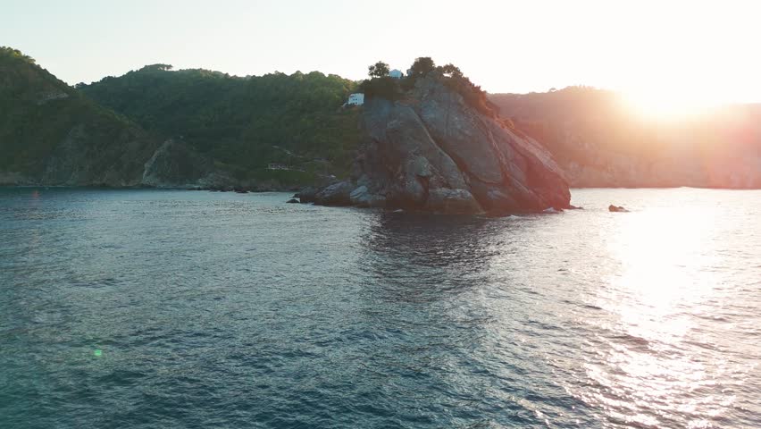 Sun setting behind a rocky island in a peaceful ocean setting with lush green hills