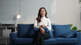 Asian woman sitting on sofa in living room holding remote control watching tv smiling and enjoying watching tv singing dancing happily relaxing vacation concept. - Powered by Shutterstock - Get 15% off with code: PIKWIZARD15
