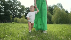 Mother helps toddler walk outside. Family bonding moment outside as toddler learns to walk. Toddler walking on grass with mother help. Family enjoys time outside. Mother's support for toddler walking. - Powered by Shutterstock - Get 15% off with code: PIKWIZARD15