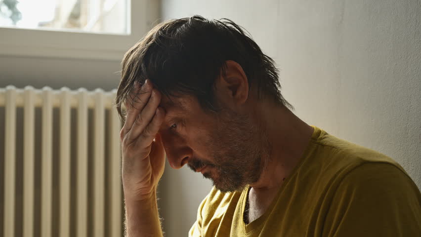 Remorse concept, regretful unkempt man at home in living room, lit by the morning sun, selective focus