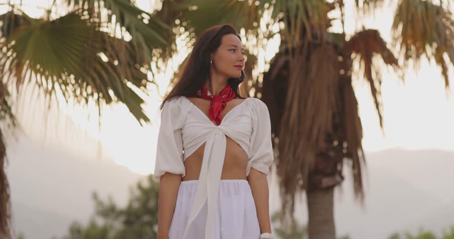 Cinematic slow-motion footage of a stylish woman in a white outfit and red scarf enjoying a tropical setting. Perfect for travel blogs, fashion promotions, and lifestyle content.