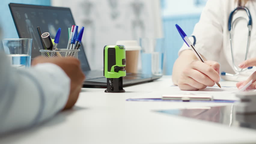General practitioner putting his stamp on a prescription document for his patient, recommending antibiotics and vitamins as medical treatment. Doctor prescribing medicaments in cabinet. Camera A.