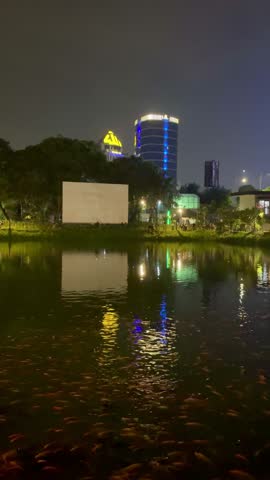 Jakarta, Indonesia, September 15, 2024. Lake with reflection of light from building lights in the water at night and background of tall buildings with colorful lights