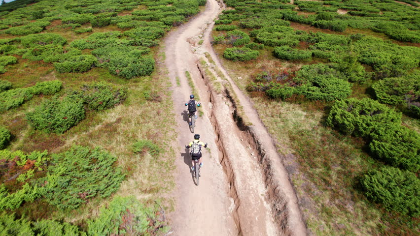 Two cyclists men riding electric bikes outdoors. Back view of male tourists biking in the mountains, wearing helmets and backpacks. Concept of sport, active leisure and nature.
