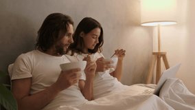 Young couple sitting in bed, eating breakfast and watching laptop. Relaxation and home leisure concept. Cinematic slow motion 4k footage, design for advertising, and social media, vlog - Powered by Shutterstock - Get 15% off with code: PIKWIZARD15