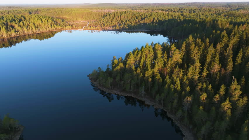 Aerial view away from a mirroring lake in the wilderness of Finland, sunset