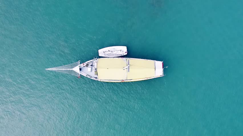 Overhead drone footage of sailboat gliding smoothly across rippled blue seascape, creating gentle waves and capturing the serene beauty of the ocean in India