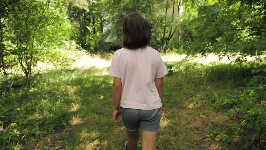 Little girl exploring the woods alone on a sunny day in nature. A young girl walks through the serene woods enjoying nature