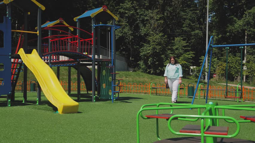 A beautiful woman in a striped shirt and white pants walks on the playground. Slow motion. Active lifestyle.
