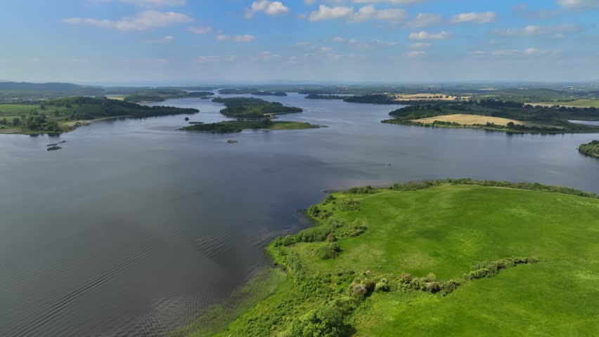 Lower Lough Erne, County Fermanagh, Northern Ireland, June 2023. Drone pushes forward establishing overview above islands on the lake sloping down to the glistening lakeshore.