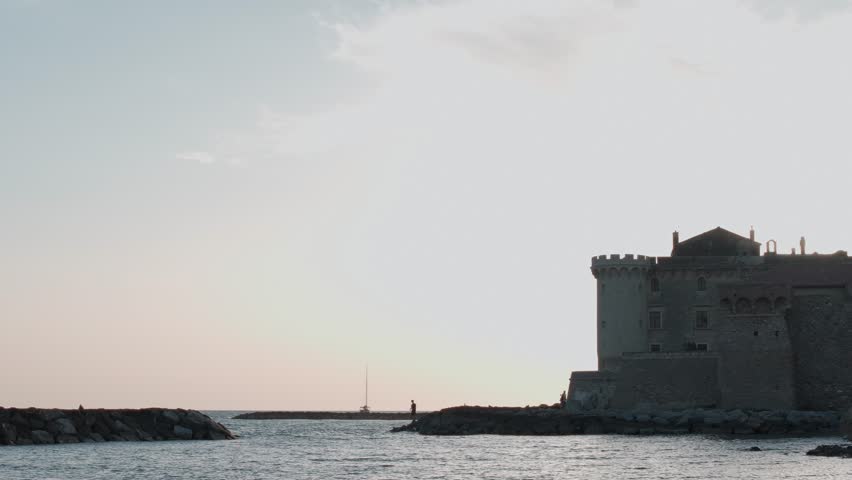 The sun sets behind a castle on the Roman coastline of Italy.