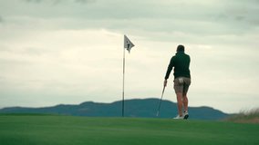Male golfer reading putting green, reading putt near pin with club in hand on Ireland links golf course on beautiful sunny day, walking in slow motion - Powered by Shutterstock - Get 15% off with code: PIKWIZARD15