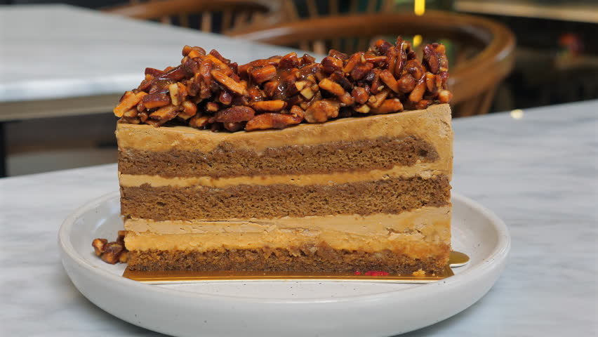 Delicious caramel and nut layered cake slice on white plate in cozy cafe setting, close-up, perfect for gourmet dessert lovers and food photography. Indulgence and Sweet Treats.