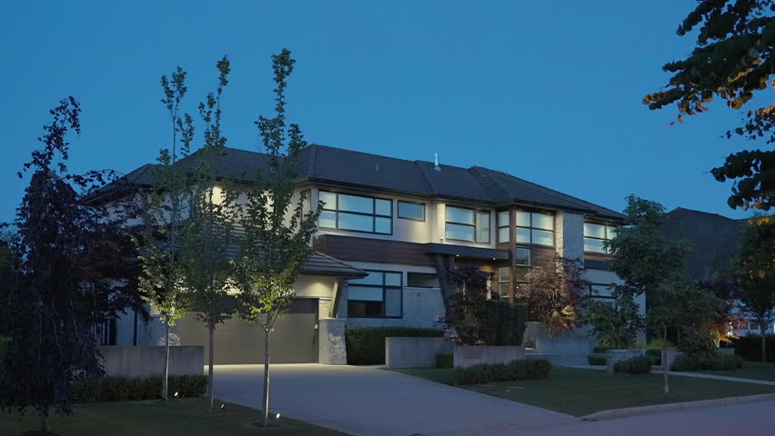 Establishing shot of two story stucco luxury house with garage door, big tree and nice landscape at night in Vancouver, Canada, North America. Night time on June 2024. ProRes 422 HQ.