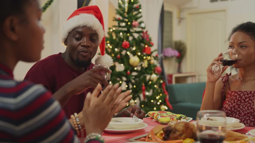 family moment during Christmas as they exchange gifts around festive dinner table. The table with Christmas-themed tableware, candles and delicious food. The room is adorned with holiday decorations.