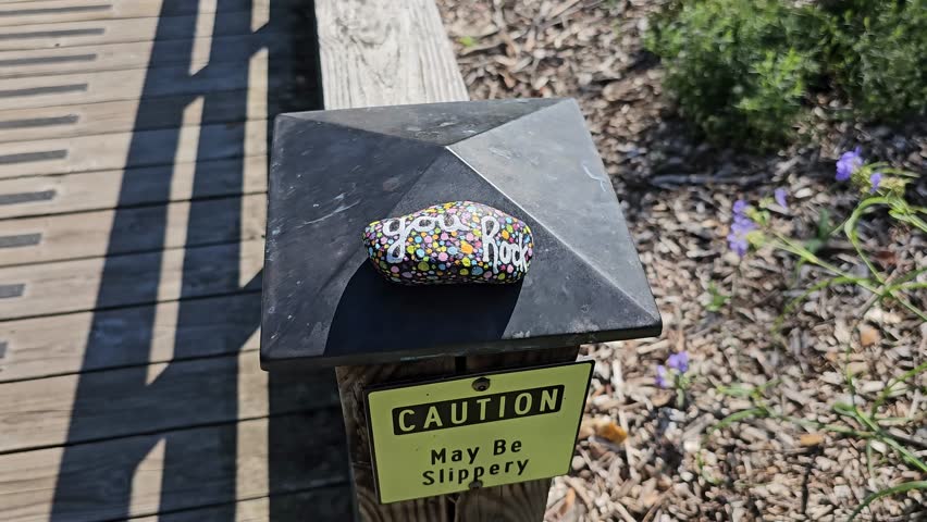 You rock kindness rock on post on walking path with slippery caution sign posted