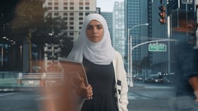 Arab Female Student in Hijab Standing Still on a City Street, Looking at Camera and Holding Textbooks. Footage with Blurred Pedestrians Walking on Timelapse Footage. Portrait of a Muslim Woman - Powered by Shutterstock - Get 15% off with code: PIKWIZARD15