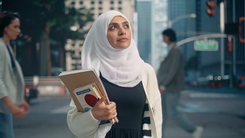Portrait of a Young Arab Female Student Wearing a Hijab, Standing on a Busy City Street, Holding Textbooks. Urban Environment Reflects Her Determination as She Balances Her Education with City Life