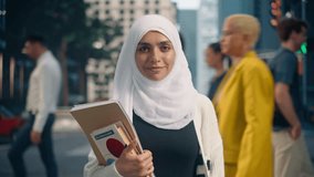 Portrait of a Young Arab Female Student Wearing a Hijab, Standing on a Busy City Street, Holding Textbooks. Urban Environment Reflects Her Determination as She Balances Her Education with City Life - Powered by Shutterstock - Get 15% off with code: PIKWIZARD15
