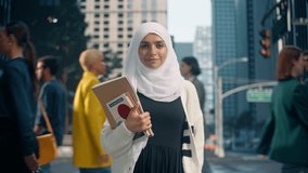 Portrait of a Muslim Female Student Wearing a Hijab, Standing on a City Sidewalk and Looking at Camera with Books in Her Hand. Diverse Young Woman Getting Education in a Big City University - Powered by Shutterstock - Get 15% off with code: PIKWIZARD15