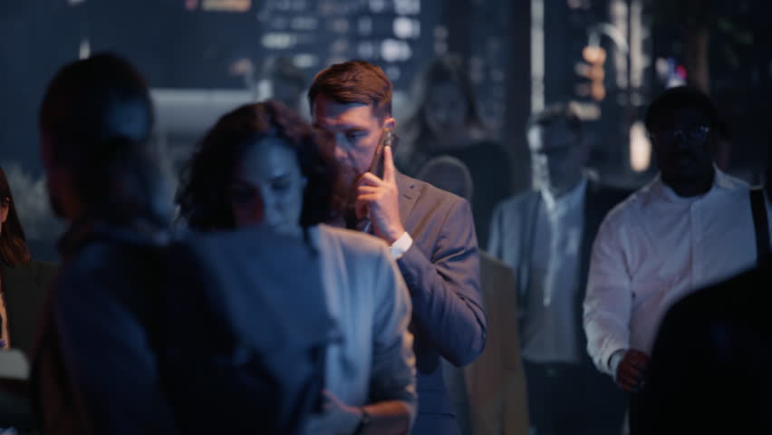 Cinematic Night Footage of a Diverse Crowd of People Walking Along a City Street, Representing a Range of Ages and Ethnicities. Men and Women Using Their Smartphones or Having Conversations
