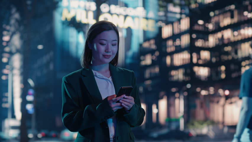 Smiling Asian Female Professional in a Stylish Outfit Standing at an Avenue, Glancing Down at Her Smartphone. Diverse Girl is Reading Through Her Latest Messages, Replying and Checking News
