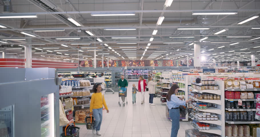 Families and Individuals from Various Backgrounds Shop Together in a Busy Supermarket. Customers Pick Up Canned Food and Packaged Goods while Comparing Prices and Checking Their Grocery Lists