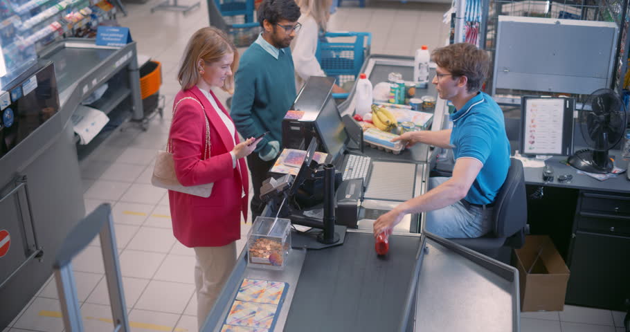 Male Cashier Scans Groceries at the Checkout Counter, His Hands Swiftly Moving as He Registers Each Item. He Engages with Female Customer while Ensuring a Quick and Accurate Transaction