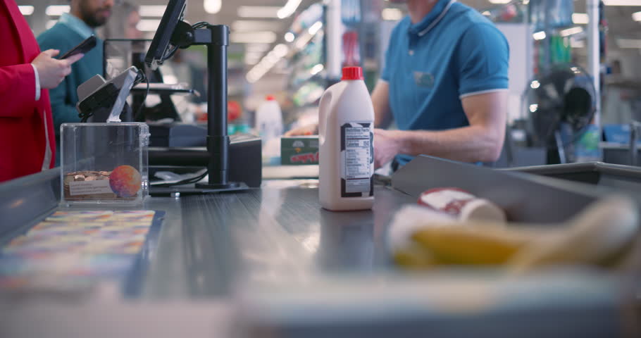 Young Male Cashier Working Behind the Register, Scanning Items at the Supermarket Checkout. His Concentration Ensures that Each Product Is Correctly Entered Into the System