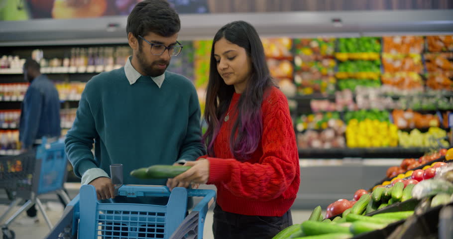 Young Indian Couple Coming to a Grocery Aisle, Carefully Selecting Fresh Ripe Tomatoes and Cucumbers From the Vegetable Shelf. Man and Female Planning to Make a Healthy Salad at Home