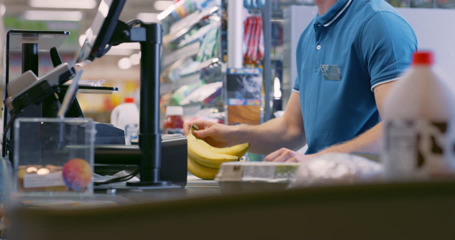 Male Cashier Scanning Product Items for Diverse Customers at a Busy Supermarket Checkout. Meat, Bananas, Eggs, Milk are Processed Efficiently, Groceries Rolling Down the Conveyor Belt