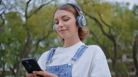 Earphones woman browsing smartphone app at green park closeup. Carefree female teenager listening music in headphones looking cellphone screen. Stylish girl hipster enjoy song relaxing on street alone - Powered by Shutterstock - Get 15% off with code: PIKWIZARD15