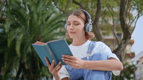 Serene woman holding book in headphones enjoying peaceful hobby in green park closeup. Relaxed girl immersed in literature and knowledge at street. Casual zoomer reading novel in earphones outdoors. - Powered by Shutterstock - Get 15% off with code: PIKWIZARD15
