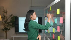 Asian businesswoman stands holding a pen and thinking. Analyze data Come up with a topic for the meeting and write it on colored sticky notes. Event planning concepts Brainstorming. - Powered by Shutterstock - Get 15% off with code: PIKWIZARD15