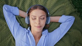 Closed-eyes woman listening music in headphones relaxing at picnic blanket closeup. Serene lady enjoying earphones sound lying green grass. Peaceful girl napping on nature feeling contentment alone. - Powered by Shutterstock - Get 15% off with code: PIKWIZARD15