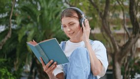 Peaceful girl reading literature in headphones sitting calmly in park closeup. Carefree woman listening music in earphones flipping book pages sunny day. Relaxed teenager enjoying intellectual hobby. - Powered by Shutterstock - Get 15% off with code: PIKWIZARD15
