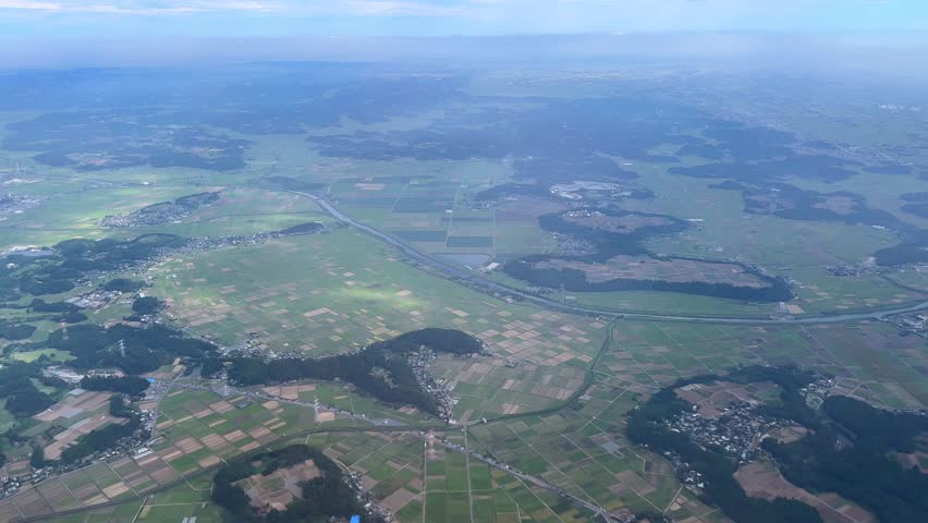 Expansive countryside with farmland and distant towns under a clear sky, aerial view