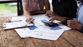 Team business discussing data at meeting. Colleagues collaborating over financial documents and charts, using a calculator, at a wooden table. Brainstorming, strategy analysis and business planning. - Powered by Shutterstock - Get 15% off with code: PIKWIZARD15