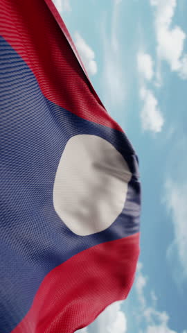 Wavy flag of Laos blowing in the wind in slow motion. Waving colorful Laotian flag team symbol abstract vertical background. Blue sky with clouds. World countries flying flags concept