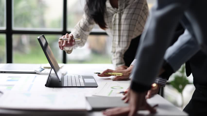 Businesswoman collaborating on data analysis during office meeting. Three businesswomen analyzing charts and graphs on a laptop during a collaborative office meeting, discussing and pointing at data.