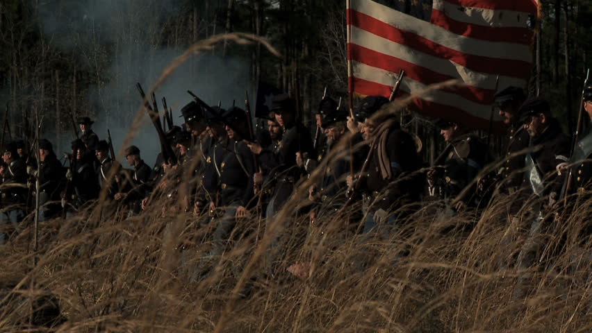 FLORIDA - FEBRUARY 2013 - large-scale, epic Civil War anniversary reenactment -- in the middle of battle.  Smokey Battlefield as Union Infantry advances into battle with flag flying in tall grass.
