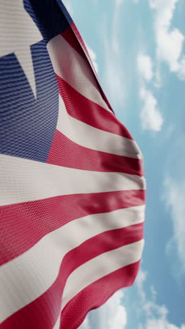 Wavy flag of Liberia blowing in the wind in slow motion. Waving colorful Liberian flag team symbol abstract vertical background. Blue sky with clouds. World countries flying flags concept