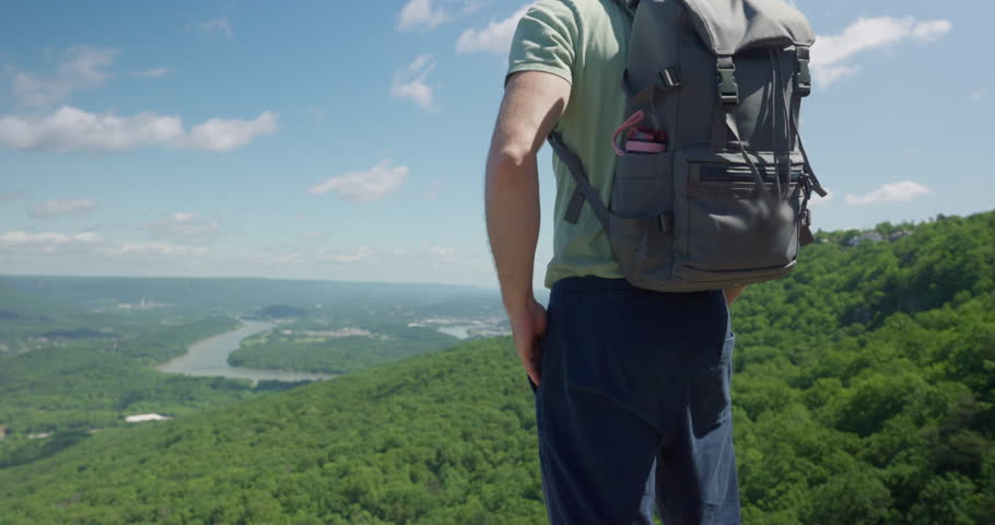 Young man standing on top of a mountain and looking at the beautiful nature view from high up. Admiring nature standing with confidence. Proud to have reached the summit. Life goal achievement