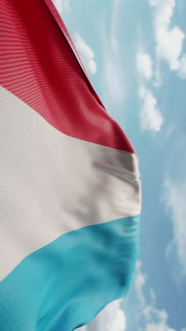 Wavy flag of Luxembourg blowing in the wind in slow motion. Waving official Luxembourg flag team symbol abstract vertical background. Blue sky with clouds. World countries flying flags concept