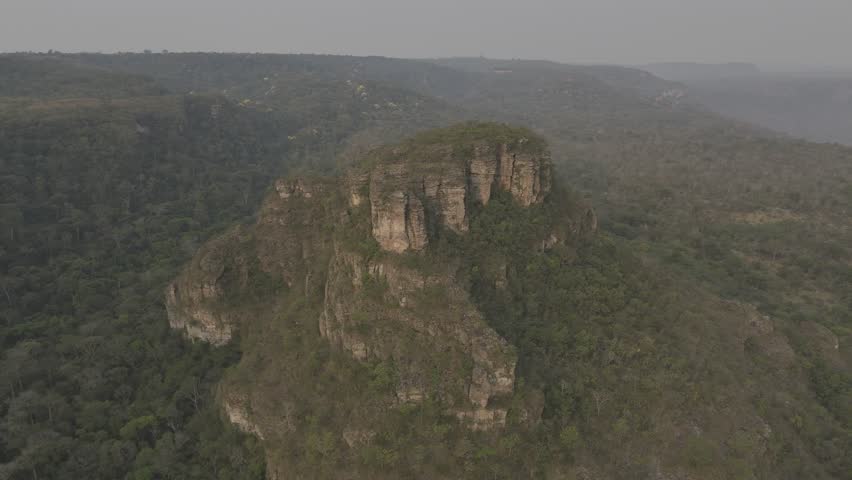 Drone orbits around large rock at sunset in a smokey valley from forest fires near Chapada Guimarães, Mato Grosso, Brazil