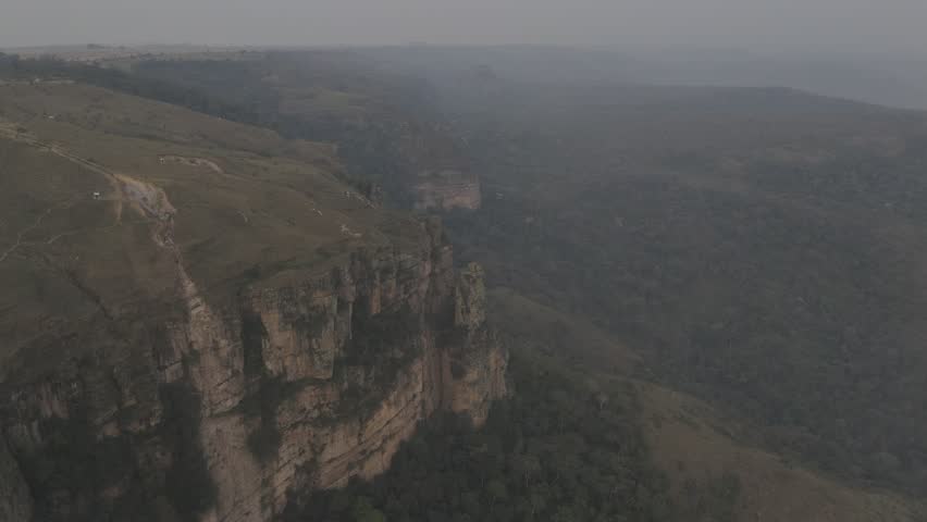 Drone lowers into smokey forest fired-filled valley at Mirante Geodésico and threads the needle between two rocks near Chapada Guimarães, Mato Grosso, Brazil
