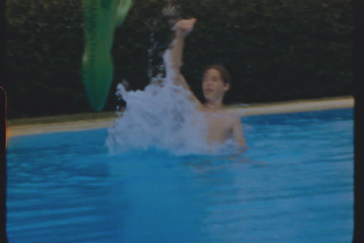 A boy swimming in a pool playing with a green inflatable alligator, filmed on 8mm film