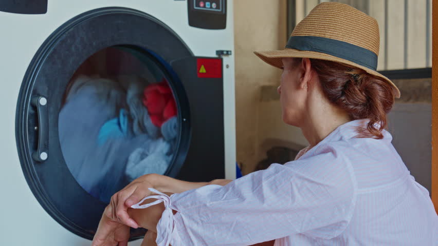 A female tourist in a hat, sitting in a laundry room, waiting for the laundry to finish washing
