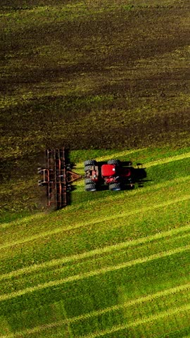 A tractor is working diligently across expansive fields, turning soil in neat rows under a clear blue sky, showcasing the vibrant green landscape of rural agriculture during a sunny afternoon.